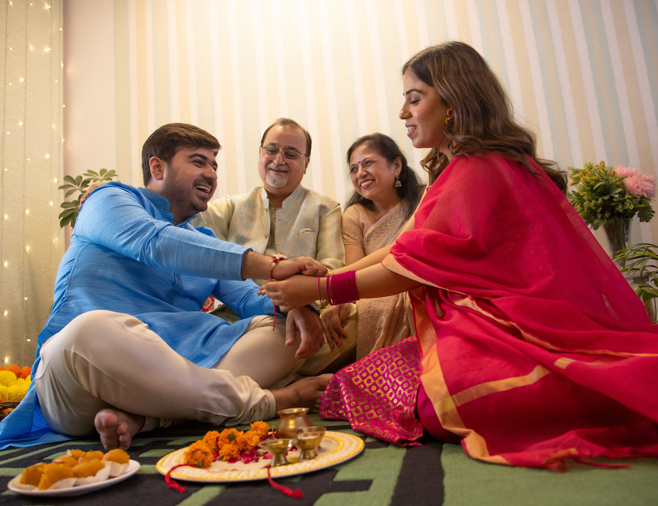 Sister tying rakhi on brother’s wrist during Raksha Bandhan celebration with family performing traditional puja rituals at home